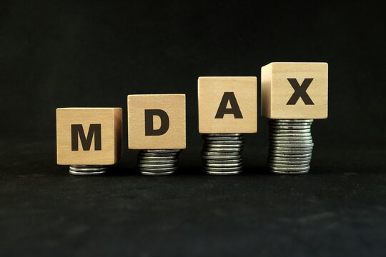 Germany stock market economy growth and recovery concept. MDAX index in wooden blocks with increasing stack of coins in black background.