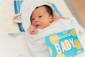 welcome babyのカードとおくるみに包まれた新生児のニューボーンフォト