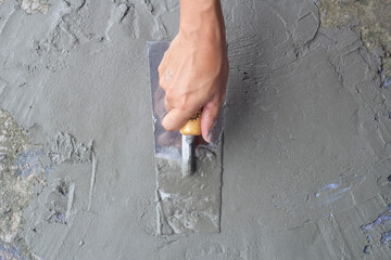 Top view of Hand of worker holding plastering trowel by leveling the concrete floor smooth. Repairing old rough floors. - obrazy, fototapety, plakaty