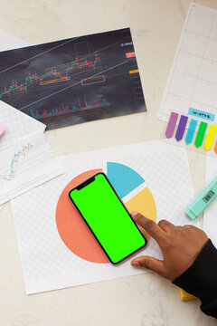 Top view smartphone and hand with green screen empty screen is on top of desk table with lots of papers 