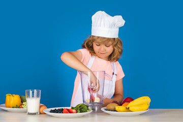 Portrait of a 7, 8 years old child in cook cap and apron make smoothie fruit salad and cooking food in kitchen. Cute little blonde happy smiling chef.