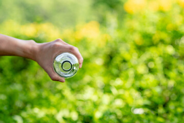 Hand holding Glass bottle for reuse or recycling with green blurred background.