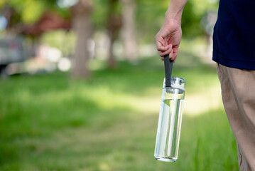 Hand holding a clean drinking water bottle. Plastic bottle of drinking water with green blurred...