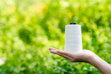 Hand holding Raw White Polyester FDY Yarn spool, Polyester Filament Yarn spool.PET fiber Yarn,spun polyester sewing thread with blurred green background