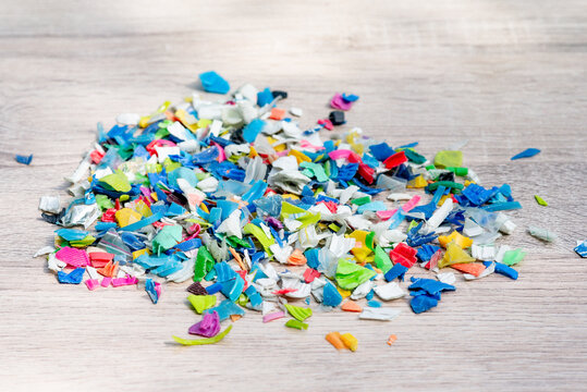 A Pile of PET bottle flakes, Plastic bottle crushed, Small pieces of cut colorful plastic bottles on wooden table
