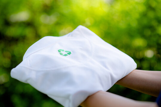 Hand holding a shirt made from recycled materials. Holding a white shirt with recycle symbol on the shirt with green blurred background.