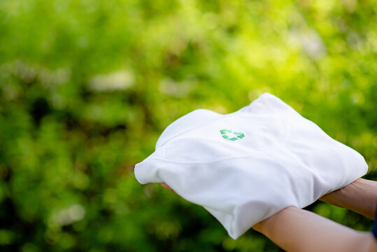 Hand holding a shirt made from recycled materials. Holding a white shirt with recycle symbol on the shirt with green blurred background.