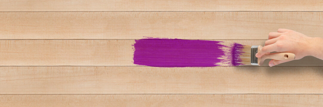 Close-up Of A Brush In The Hand Of A Person Painting A Wooden Board, Hobby And Renovation Concept. A Man's Hand Paints A Wooden Wall Or Floor Purple. View From Above