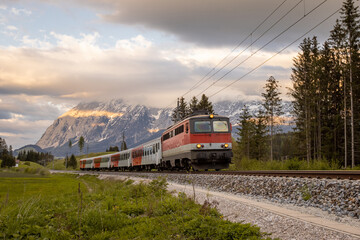 Fototapeta na wymiar Austrian train rushing past the camera with an electric locomotive of older type and four carriages on early evening..