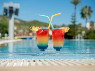 glasses with summer bright cocktails and drinking straws stand by the pool