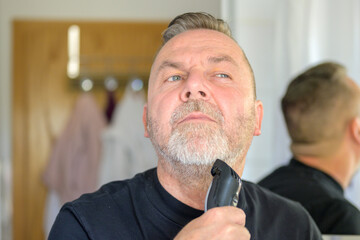 Senior man using an elecrric trimmer to trim his beard