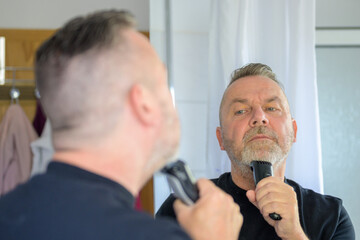 Middle-aged man trimming his beard in the mirror