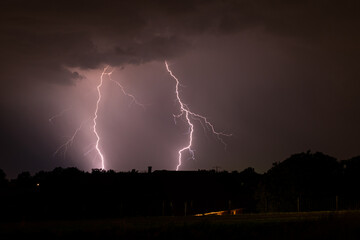 Double lightning strike behind a row of trees during a nighttime thunderstorm