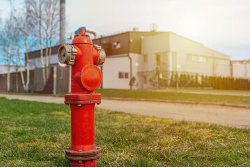 Fototapeta na wymiar Single red fire hydrant on green sunset lawn.In a background factory.Autumn,spring,summer day.Copy space.