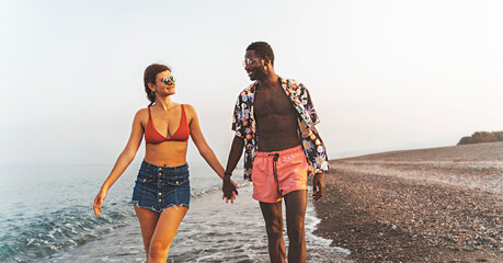 Multiethnic couple walking in the beach - lifestyle concept of multiracial young people having fun in the summer