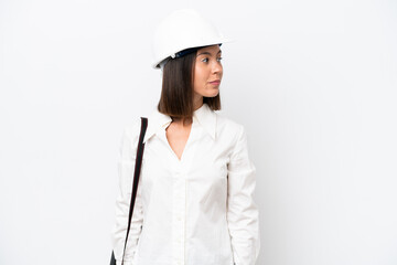 Young architect woman with helmet and holding blueprints isolated on white background looking to the side