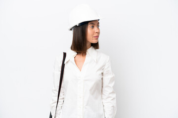 Young architect woman with helmet and holding blueprints isolated on white background looking to the side