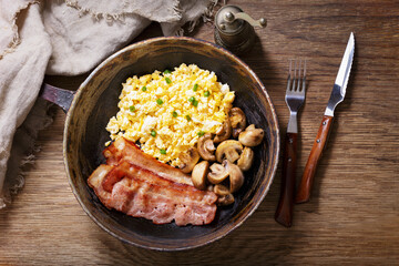 Breakfast with pan of scrambled eggs, bacon and mushrooms
