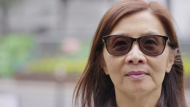 Portrait of senior Asian female in sunglasses looking to camera, in slow motion