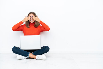 Young caucasian woman sitting on the floor with a laptop covering eyes by hands