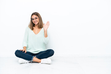 Fototapeta premium Young caucasian woman sitting on the floor isolated on white background saluting with hand with happy expression