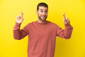 Fototapeta premium Handsome blonde man over isolated yellow background with fingers crossing and wishing the best