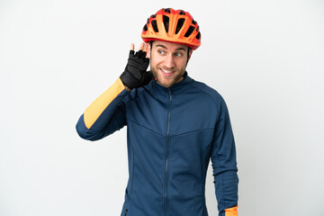Young cyclist man isolated on white background listening to something by putting hand on the ear