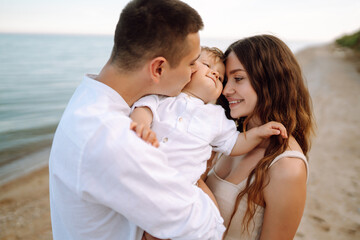 Fototapeta premium Cute family are having fun on the beach. Father, mother and child against the background of the blue sea and sky. Travel, active lifestyle, vacation, rest concept.