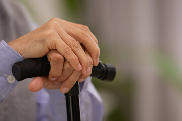 Close up hand.Asian Elderly man holding walking stick for physiotherapy.Sitting on sofa after walking in morning.