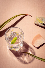 Glass with water in sunshine, light beige background. Summer gin cocktail with aloe vera and lime....