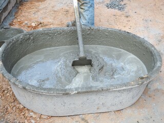 Workers use spade mixing wet cement in cement mixing basin.