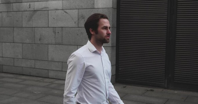 TS Young bearded Caucasian businessman while walking along near the modern business building in outdoor. Busy day in a big city.