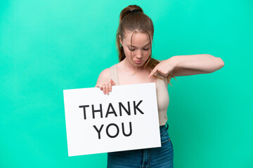 Young caucasian woman isolated on green background holding a placard with text THANK YOU and  pointing it