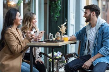 Group of cool friends sharing a brunch together while talking and looking the smartphone on the healthy coffee shop terrace.