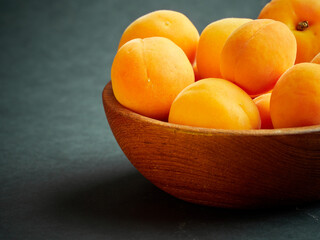 Bright ripe apricots in a wooden bowl on a dark background