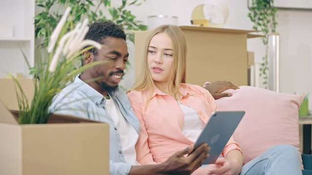 Joyful multiethnic couple browsing on tablet, buying furniture for a new home