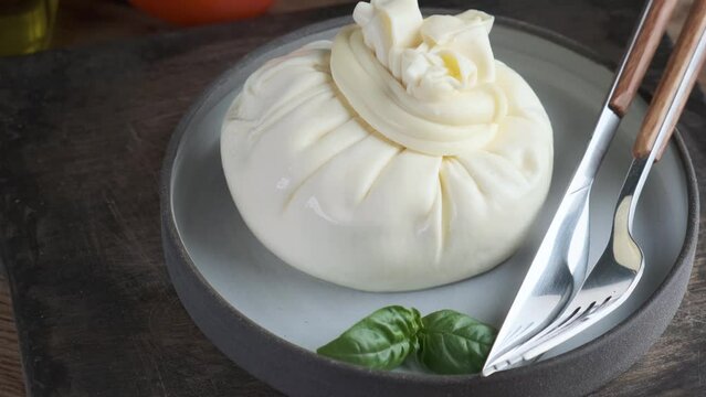 Italian burrata cheese in a plate with cutlery and basil. Dairy food. Italian appetizer. 4k video