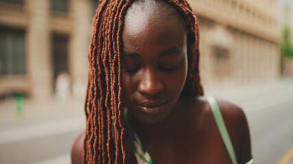 Close-up of beautiful woman with African braids raising her head and looking at the camera with...