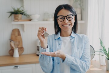 Smiling positive spanish woman is showing house key in her hand. Happy real estate owner.