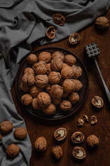 Many whole walnuts on a dark ceramic plate and grey napkin on a wooden background.