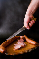 A man cuts a sausage. Sausage cut into pieces lies on a wooden floor. Homema desausage. Meat products on a black background. 