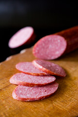 Salami sausage cut into slices. Salami on a wooden board. Sausage on a black background. A knife that cuts sausage. salami on wooden board. salami on wooden table. salami on a board.