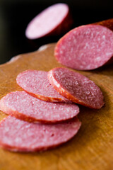 Salami sausage cut into slices. Salami on a wooden board. Sausage on a black background. A knife that cuts sausage. salami on wooden board. salami on wooden table. salami on a board.