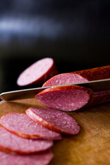 Salami sausage cut into slices. Salami on a wooden board. Sausage on a black background. A knife that cuts sausage. salami on wooden board. salami on wooden table. salami on a board.