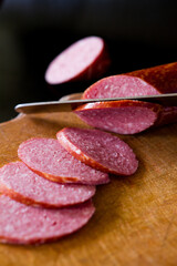 Salami sausage cut into slices. Salami on a wooden board. Sausage on a black background. A knife that cuts sausage. salami on wooden board. salami on wooden table. salami on a board.