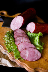 Ukrainian sausage. Sausage cut into slices lies on lettuce leaves. Sausage on a wooden board. Sausage on a black background. Kyiv sausage.