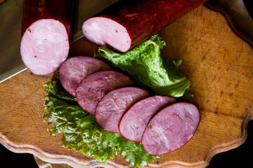 Ukrainian sausage. Sausage cut into slices lies on lettuce leaves. Sausage on a wooden board. Sausage on a black background. Kyiv sausage.