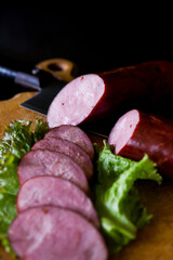 Ukrainian sausage. Sausage cut into slices lies on lettuce leaves. Sausage on a wooden board. Sausage on a black background. Kyiv sausage.
