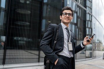 Fototapeta premium A financier uses a phone, writes a message to a colleague, a man with glasses goes to the office to work, in a business suit