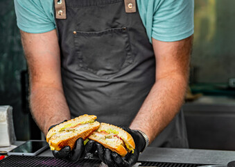 man chef hold on hand sandwich with cheese, vegetables and sause on street food kitchen